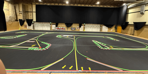Wide view of an indoor carpet RC track with green edging, red and white kerbs and numbered corners.
